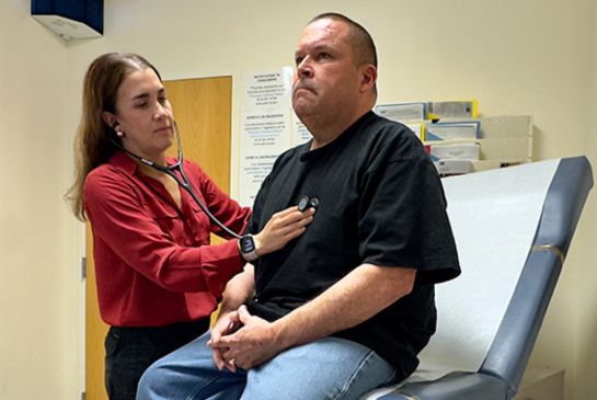 A doctor listens to her patient’s heartbeat with a stethoscope during a checkup in a medical exam room.